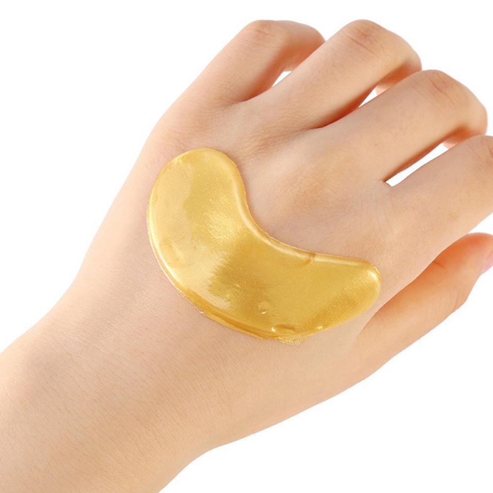 A single gold hydrogel eye patch held on the back of a hand, showing its size and shape