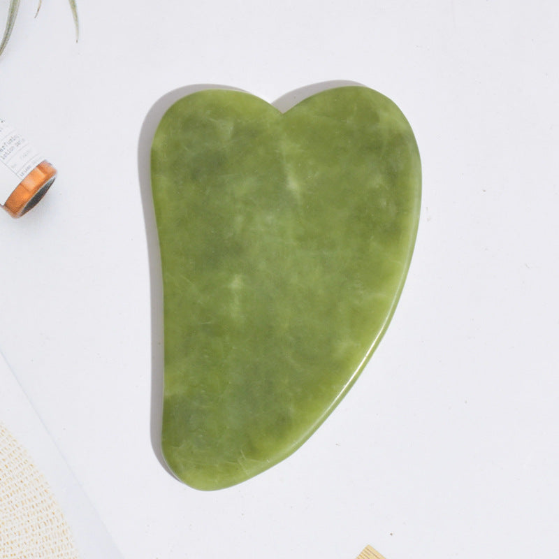 Large heart-shaped jade gua sha stone for facial massage, shown flat on a white surface