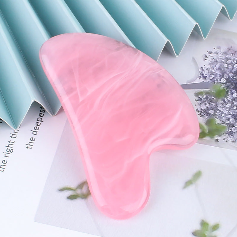 Pink heart-shaped gua sha stone for facial massage, propped against a pleated backdrop