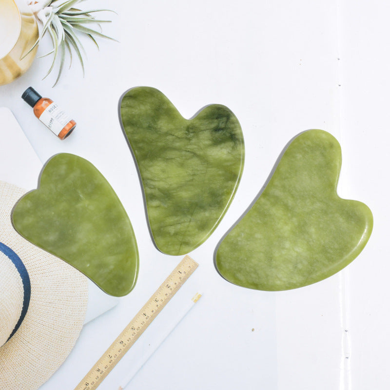 Three jade gua sha stone shapes side by side with a ruler, showing the heart, wing and contoured jawline cuts